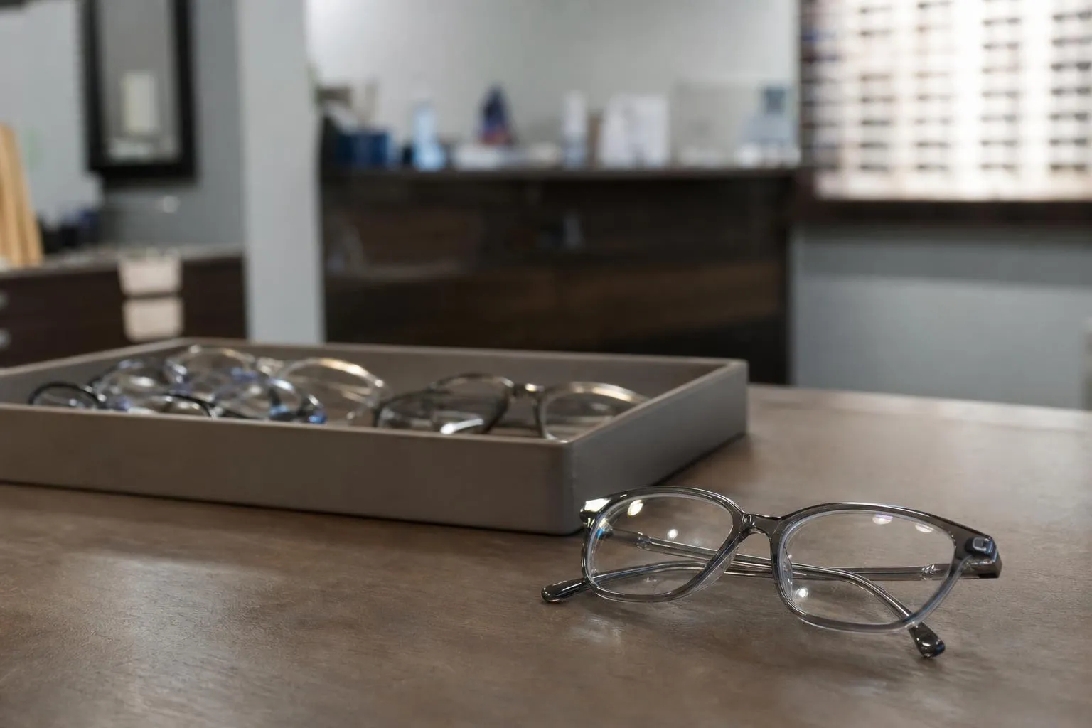 Finished prescription glasses on a dispensing table beside a tray of empty frames