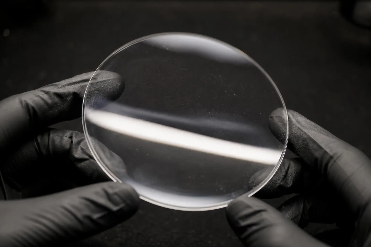 Hands tilting a clear lens under a bright lamp against a dark background