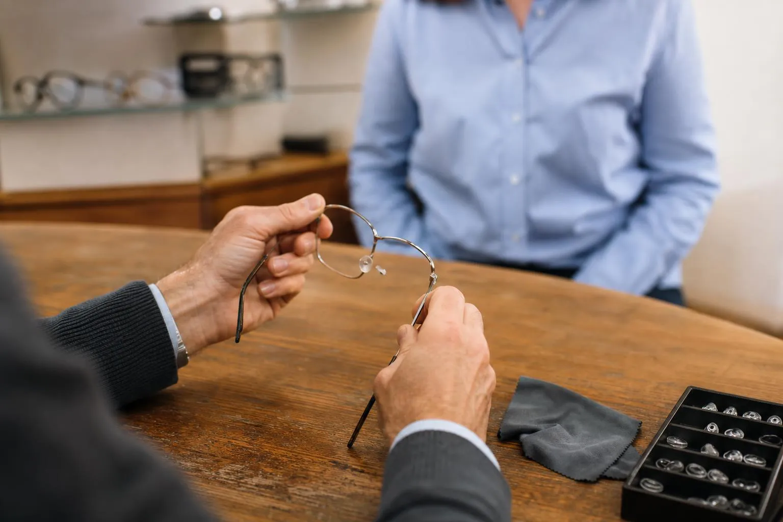 An optician’s hands adjusting the temple of a frame at a dispensing table