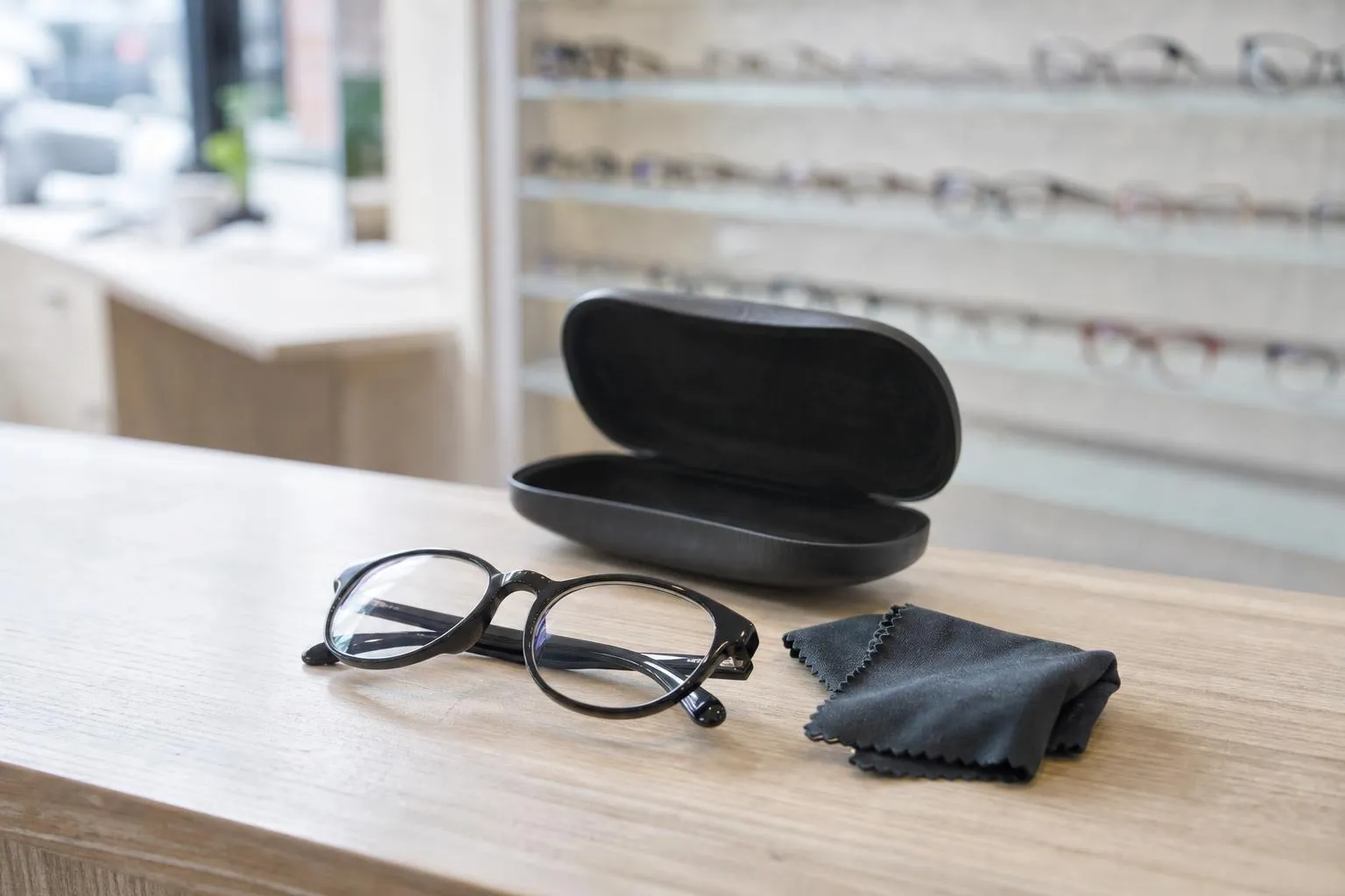 New glasses folded on a dispensing table beside an open case, a wall of frames out of focus behind