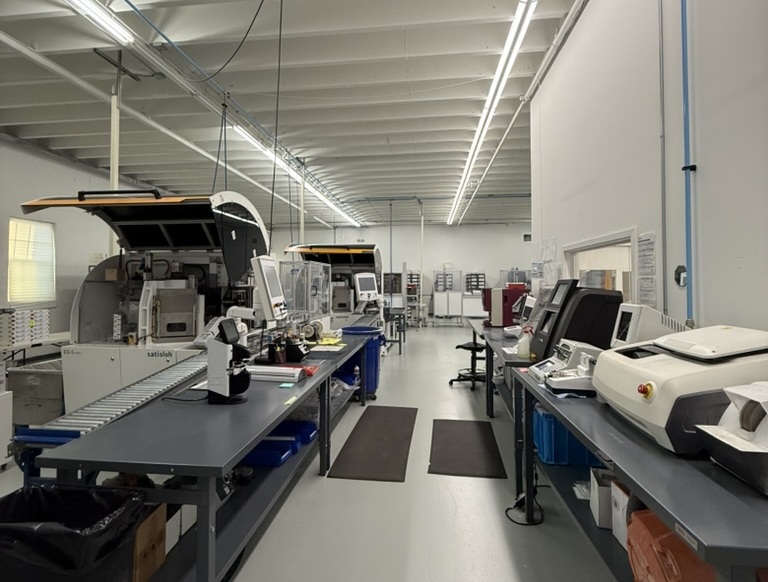 Modern Equipment at ITFIT Optical Laboratory - ITFIT Optical Laboratory Interior view of ITFIT Optical Laboratory showing a clean, organized workspace with advanced optical equipment and machinery on long workbenches under bright overhead lighting – ITFIT Optical Laboratory